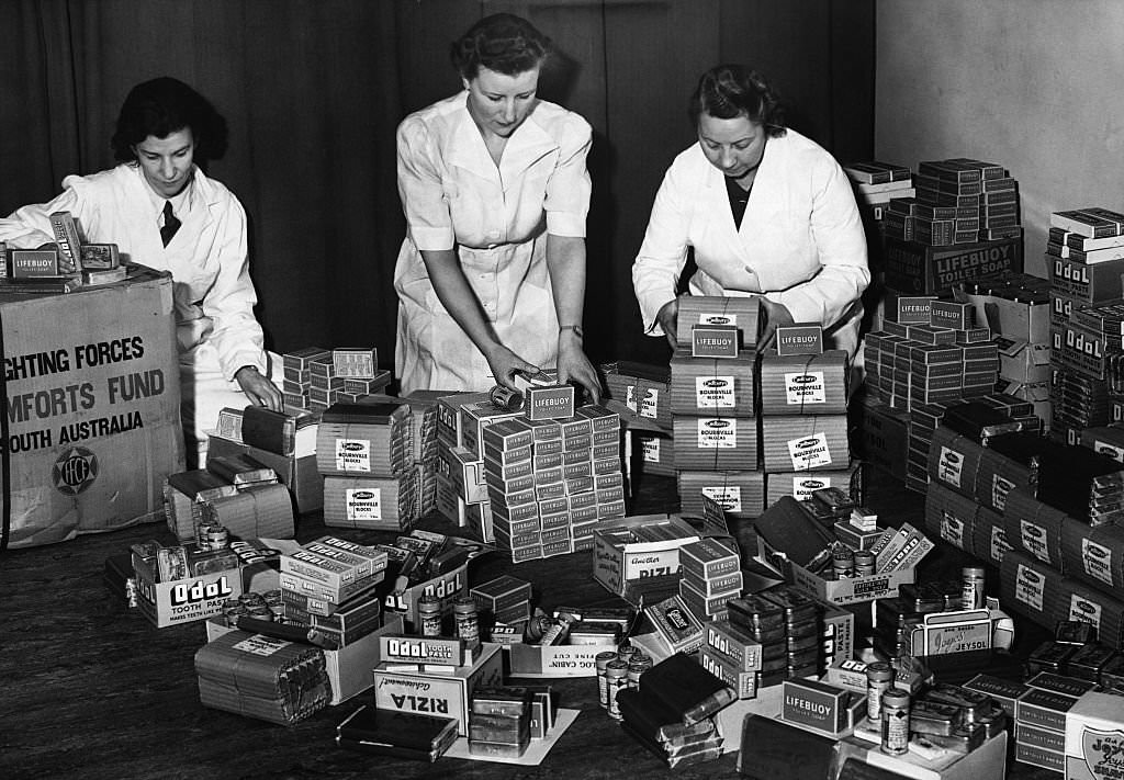 Women prepare care packages of chocolate, tobacco, cigarette papers, toothpaste, razor blades, and soaps for British troops, all gifts from the South Australian Fighting Forces Comfort Fund.