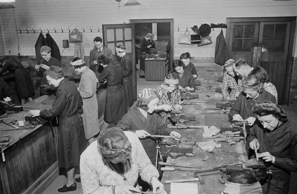Women, many wearing headscarves, use files to deburr metal held in vices in a metalworking class at the Westminster Institute in London during World War II, 28th November 1940.