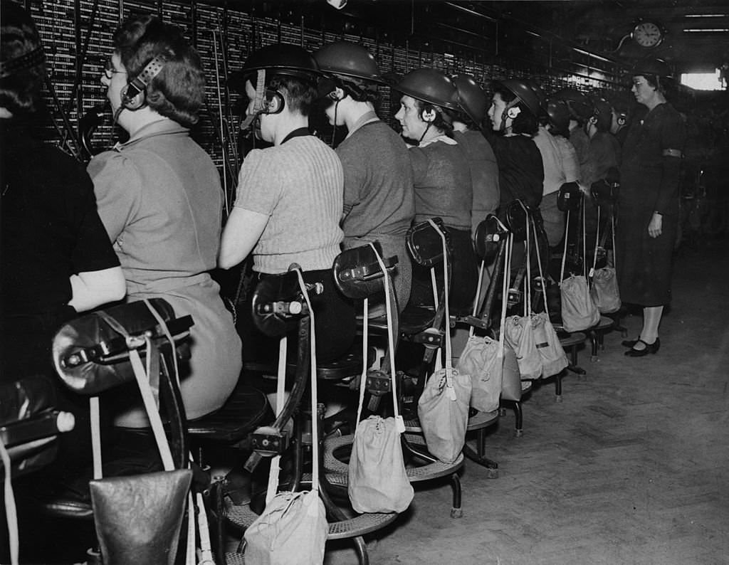 Staff at work at a major London telephone exchange wearing tin helmets during an alert.