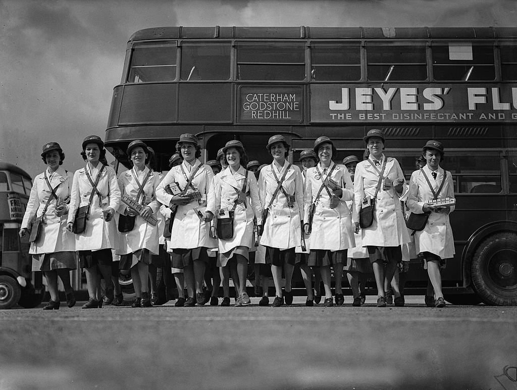 The first women bus conductors all wearing their uniforms and holding equipment as they walk to their buses at a London transport depot during World War Two