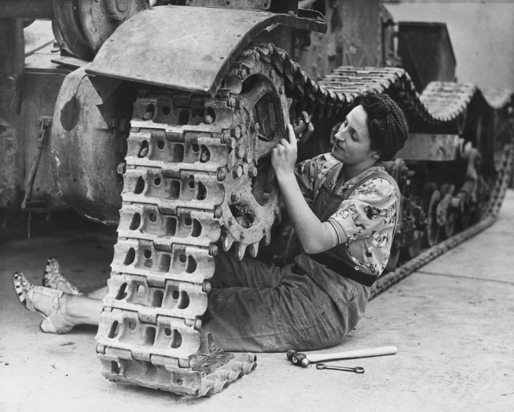 A woman war worker adjusting the tracks on a tank.