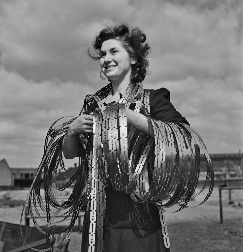 A female employee posed with strips of freshly stamped out steel razor blades yet to be being hardened, sharpened and cut at a Gillette razor blade factory in England during World War II on 12th April 1943.