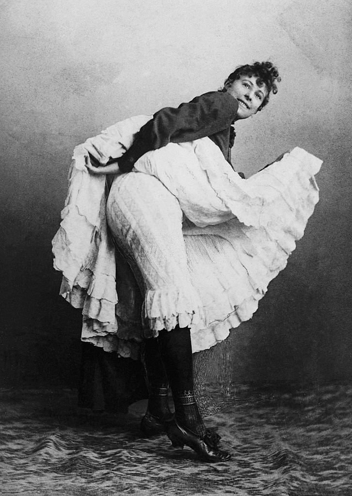 A cancan dancer lifts her skirt to reveal her bloomers, 1900s