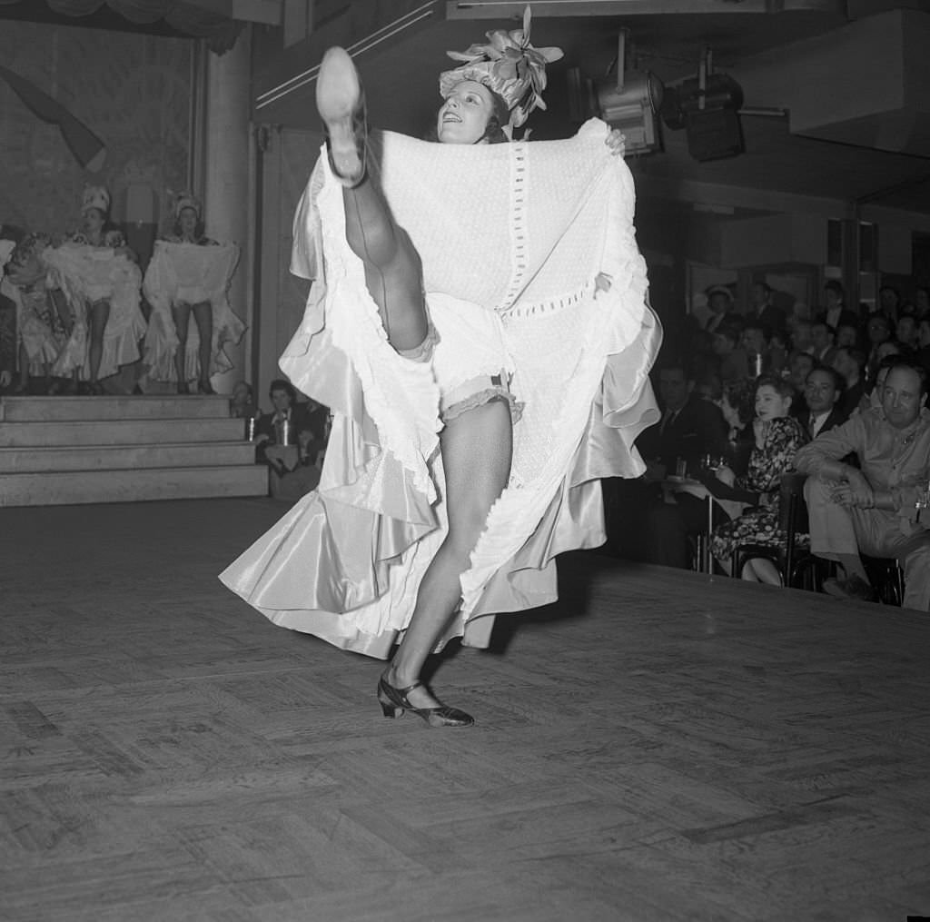 A black-stockinged, petticoated chorine demonstrates that the ever-popular Can-Can is back in Paris and the city is once again as gay as it was before the war.