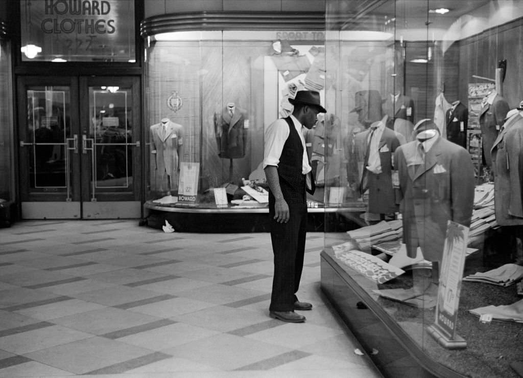 A young man in a hat window shopping at a clothing store, Chicago, Illinois, July 1941.
