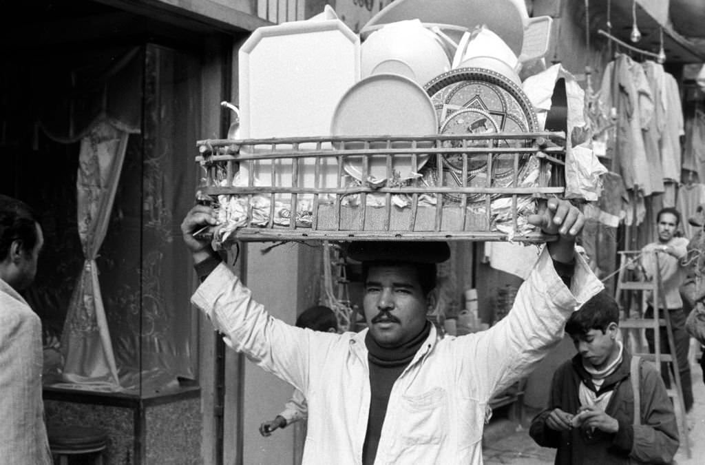A vendor carries a basket of household goods on his head at a bazaar in Cairo, 1972