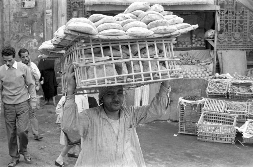 A baker carries a woven basket with flatbread on his head to a stall in a bazaar in Cairo, 1972