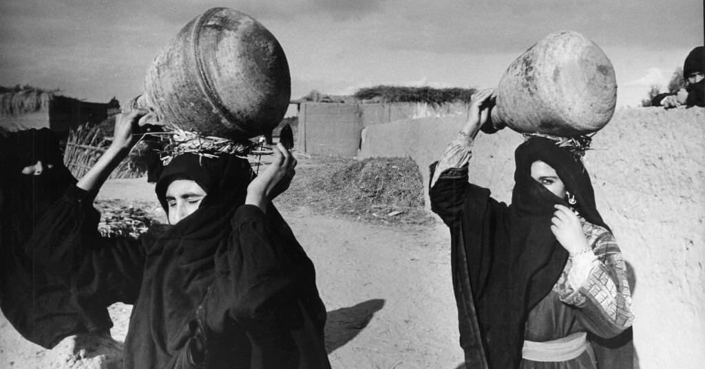 Veiled women from a village near Luxor (Egypt) carry water jars on their heads, 1972