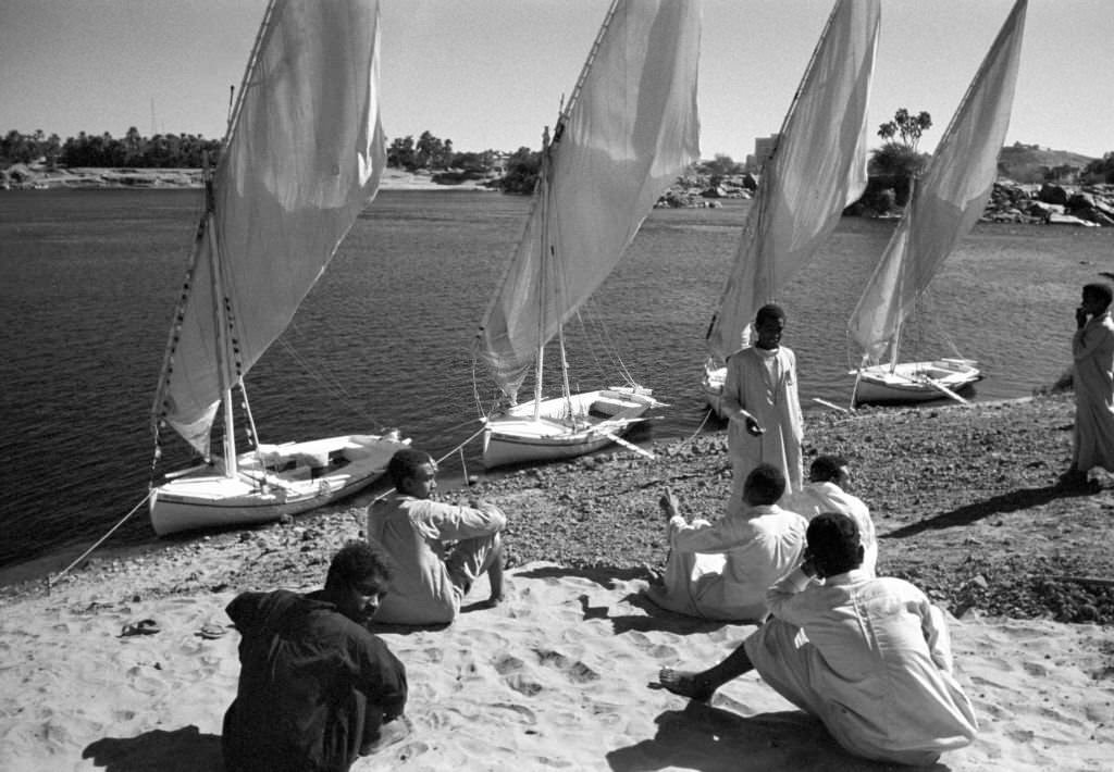 Men sit on the banks of the Nile near Aswan (Egypt) in front of small boats, so-called feluccas, 1972