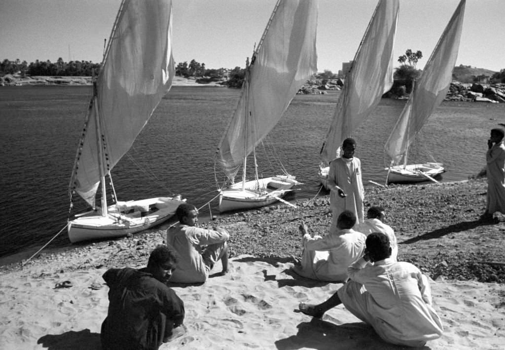 Men sit on the banks of the Nile near Aswan (Egypt) in front of small boats, so-called feluccas, 1972