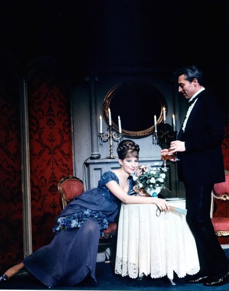 Barbra Streisand leans on a table next to a man in a scene from the film 'Funny Girl', 1968.