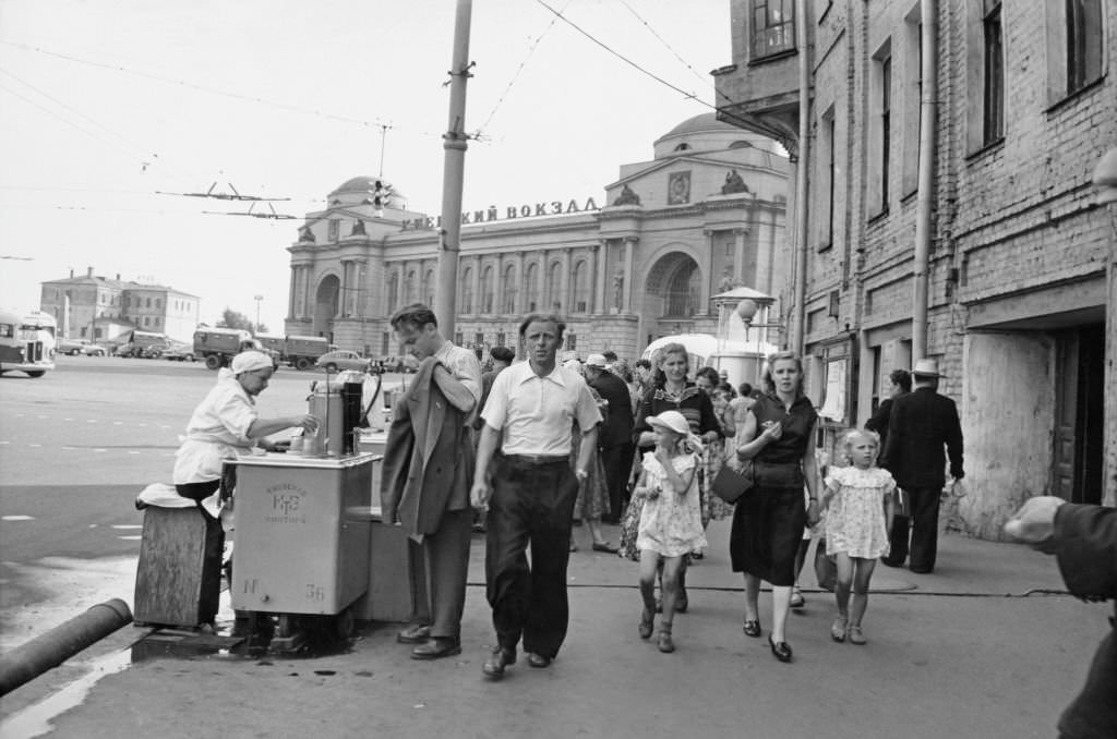 A man holds his jacket as he is served by a street vendor as pedestrians walk by a street in Kyiv, 1965