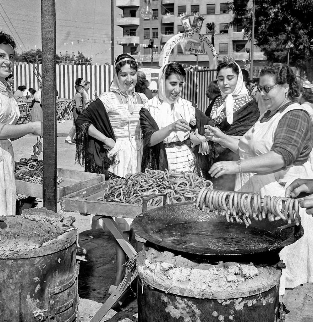 Women dressed as chulapas buy churros from a street stall in San Antonio de la Florida during the 1960s in Madrid, Spain.