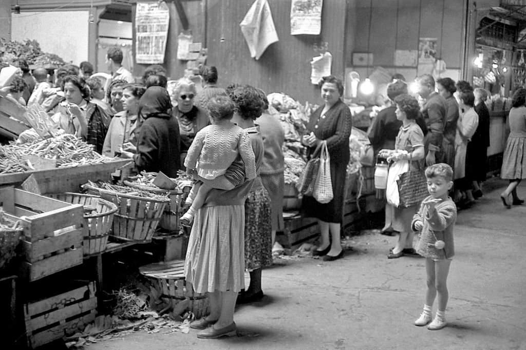 Groups of women buy vegetables at a market stall during the 1960s in Madrid, Spain.