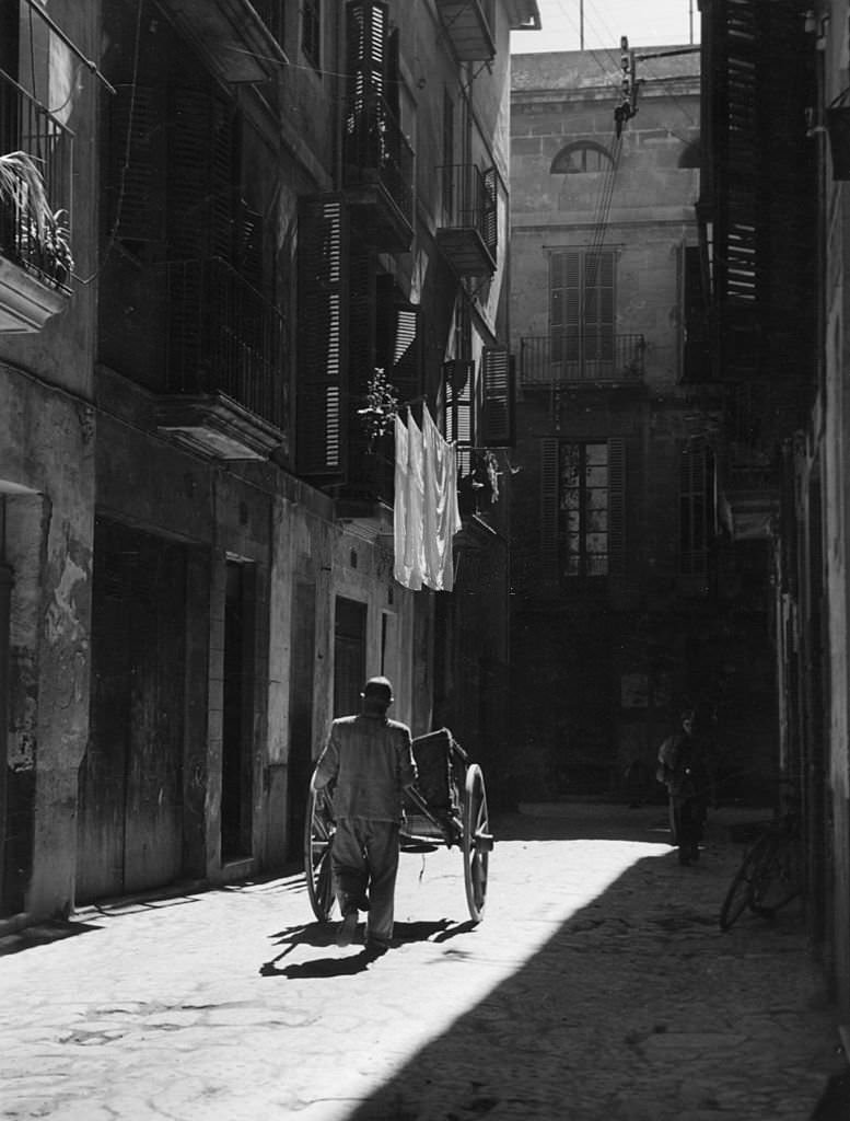 A man pushing a cart down a quiet side street in Palma de Majorca, 1950