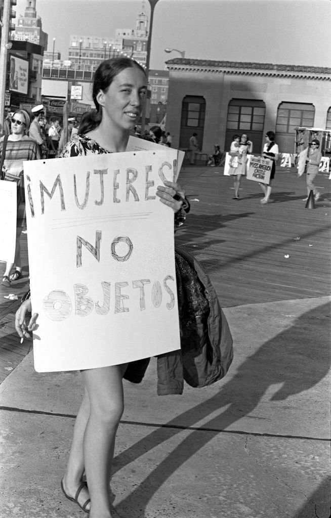 A demonstrator carries a poster that reads 'Mujeres! No Objetos' (translated as 'Women! Not Objects') as, with others, she protests the Miss America beauty pageant, Atlantic City, 1968.