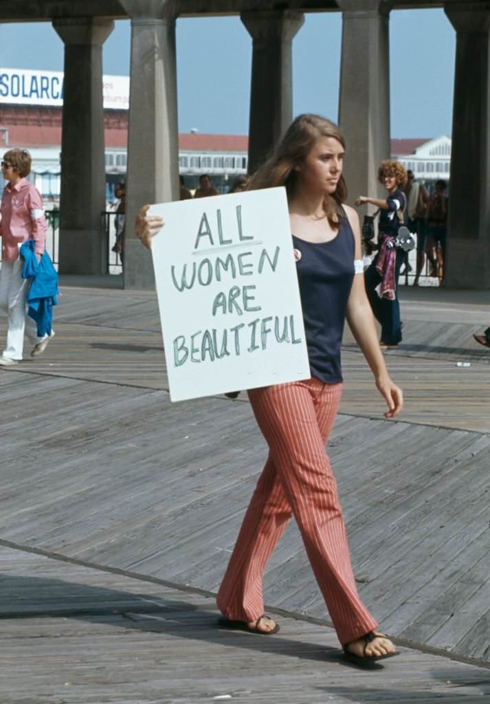 A protest against the Miss America Pageant at Atlantic City, New Jersey, 6th September 1969. A woman walks past with a sign reading 'All women are beautiful'.