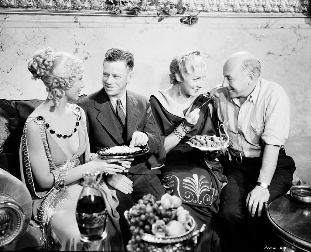 Cecil B DeMille eating food with a group of people during the making of the film 'Samson and Delilah', 1949