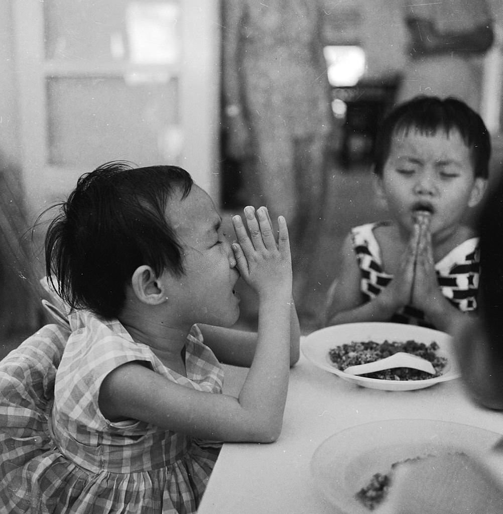 A young girl prays before eating her meal at a Red Cross run school for disabled children in Singapore, 1964