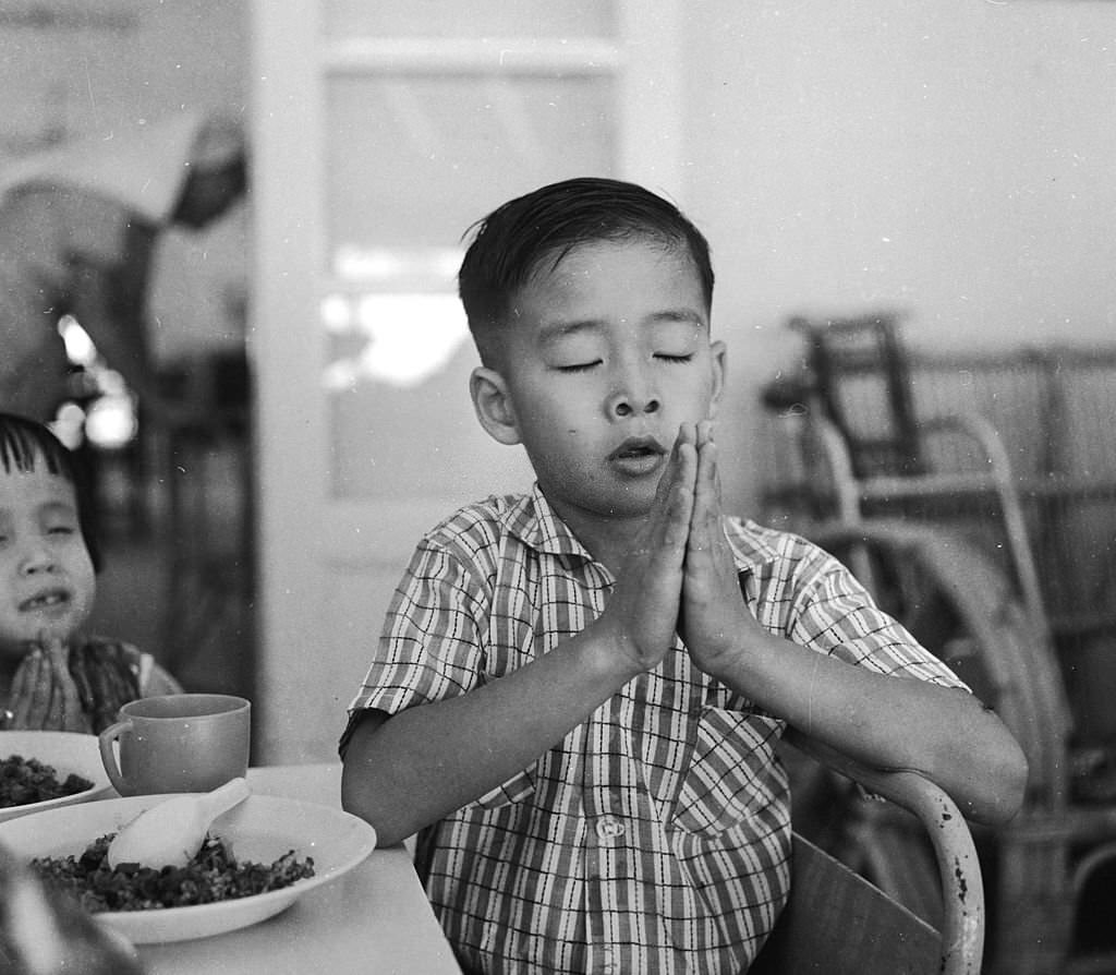 A young boy prays before eating his meal at a school for disabled children in Singapore, run by the Red Cross, 1964