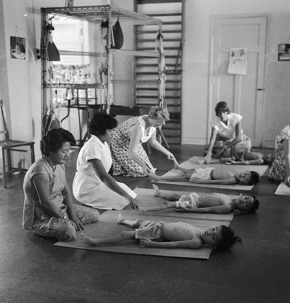 Children going through their daily exercises with the assistance of volunteers at a Red Cross school for disabled children in Singapore, 1964