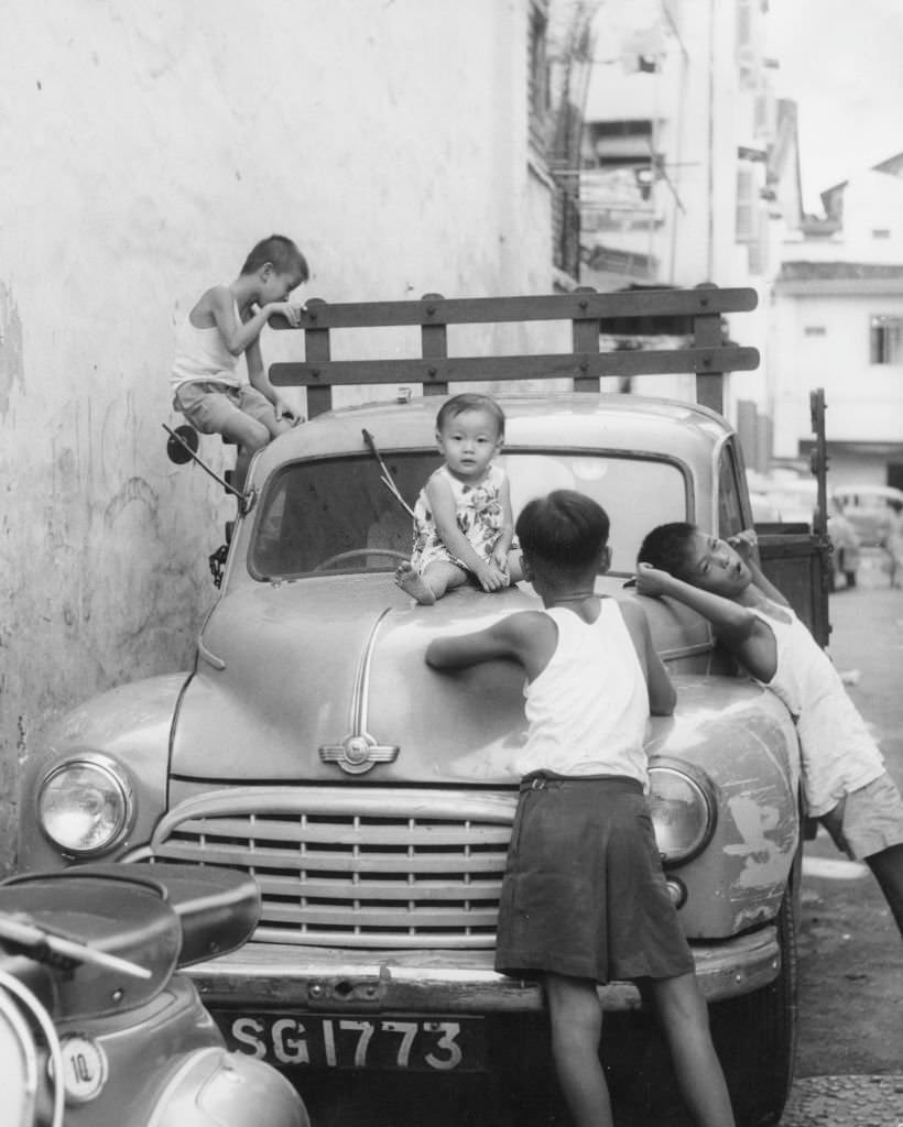 Children in Singapore clamber over a parked van, 1962