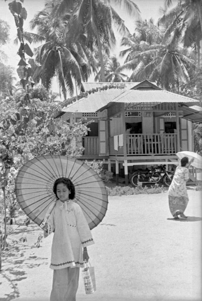 Asian little girl walking protecting herself from the sun under a parasol, Singapore, 1962