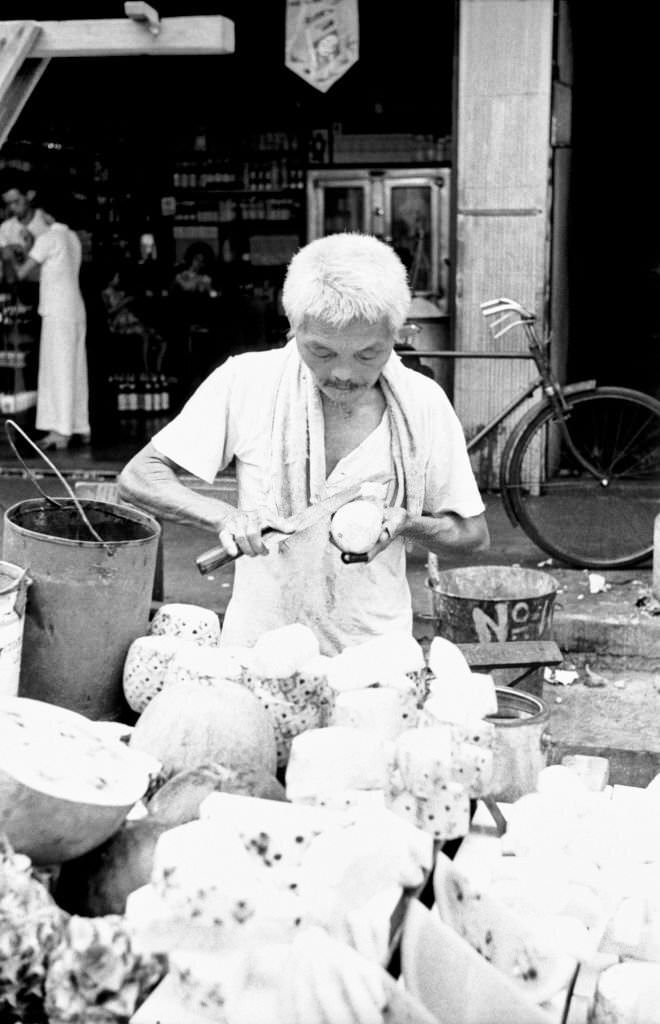 Street vendor peeling fruits in an outdoor food market, Singapore, 1962