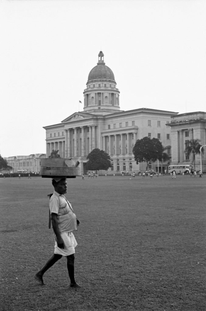 Man carrying items on the head at the park nearby the Old Supreme Court of Singapore, 1962