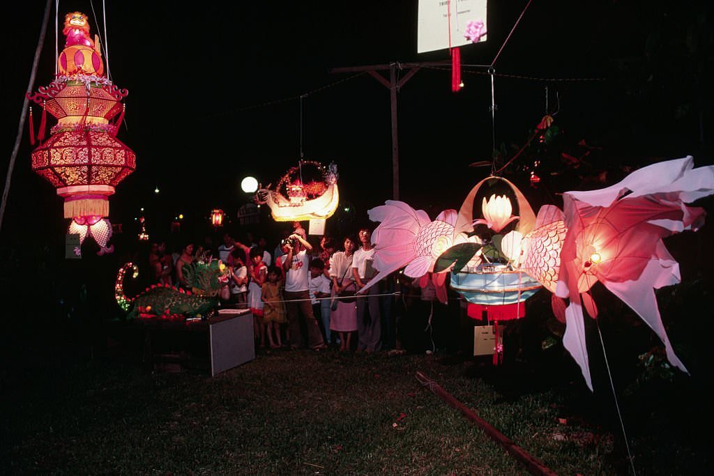 Several onlookers examine paper lanterns shaped like dragons, fish, boats, and other things at a paper lantern festival in Singapore.