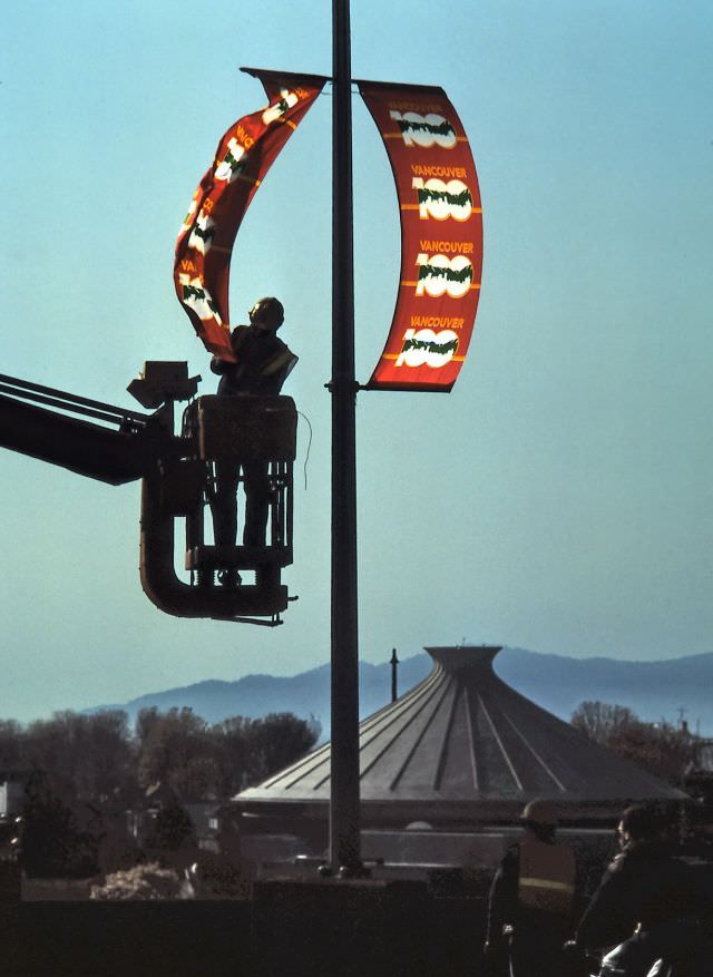 Workman putting up banners on Burrard Street Bridge in Vancouver for the city's 100th Birthday, 1986