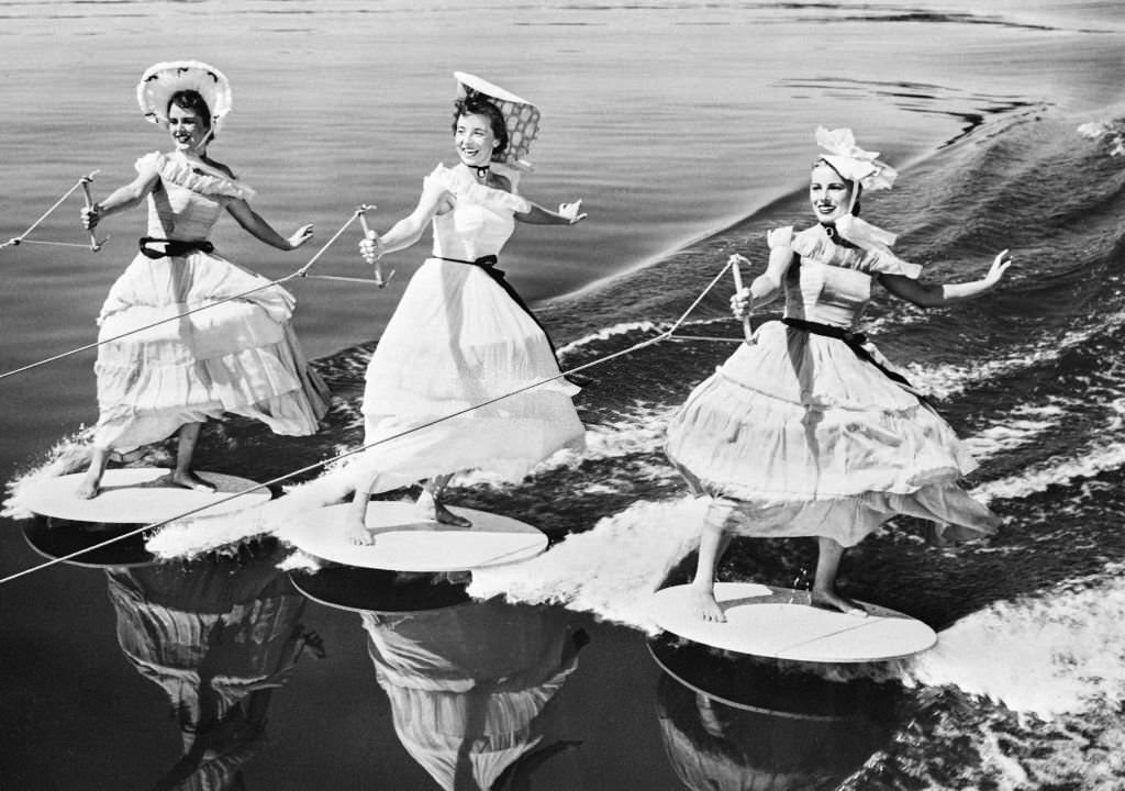 Young female skiers dressed in a period costume and wearing hats parade on the water of Cypress gardens, in the 1930s