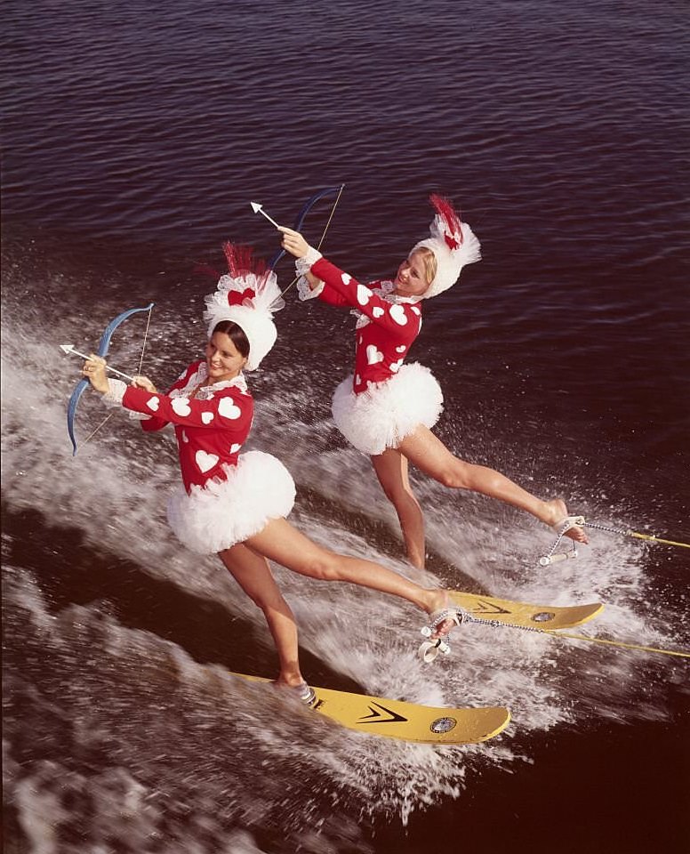 Two pretty cupids take to the water in search of their Valentines at Cypress Gardens, Florida. They're performing a difficult backward on their water skis as they aim for their sweethearts