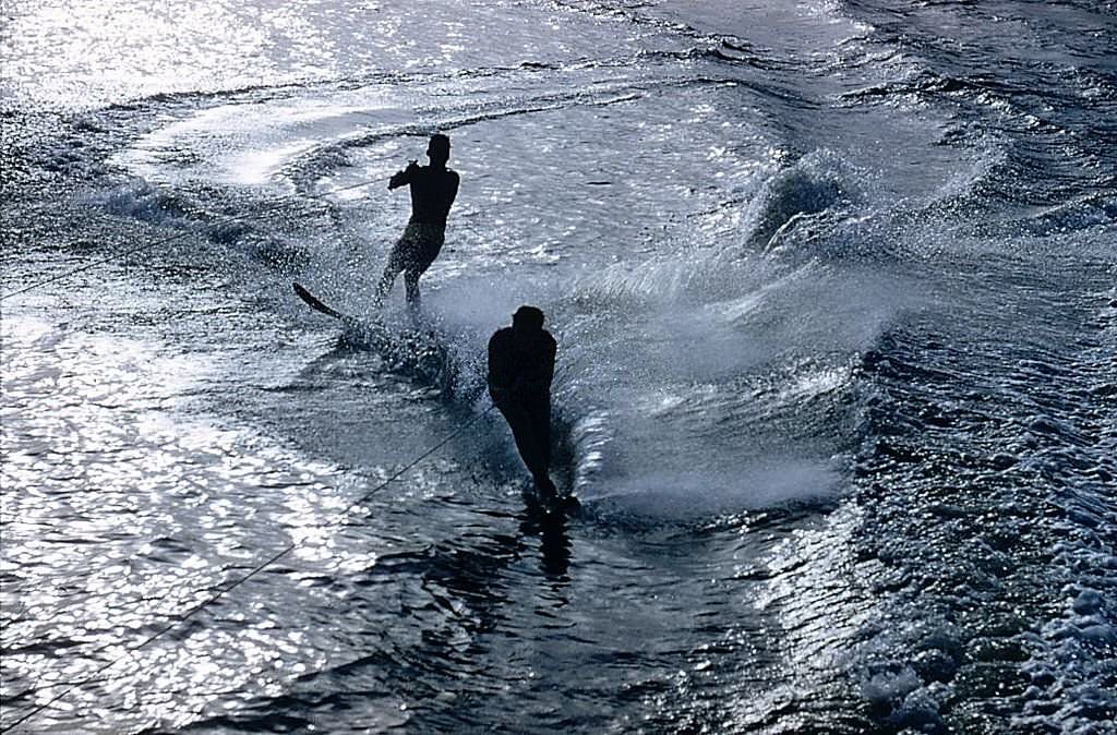 Water-skiers at Cypress Gardens, Florida are silhouetted against silver water, 1970