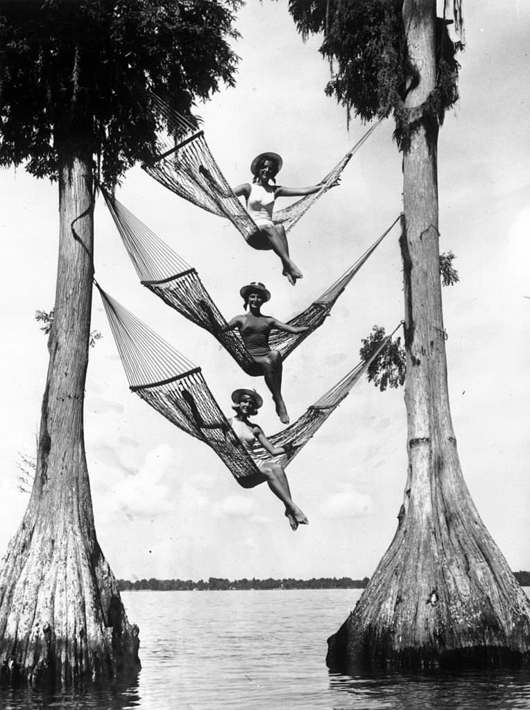 Three sunbathers balance in three hammocks suspended high up above the water in Cypress Gardens, Florida, 1966
