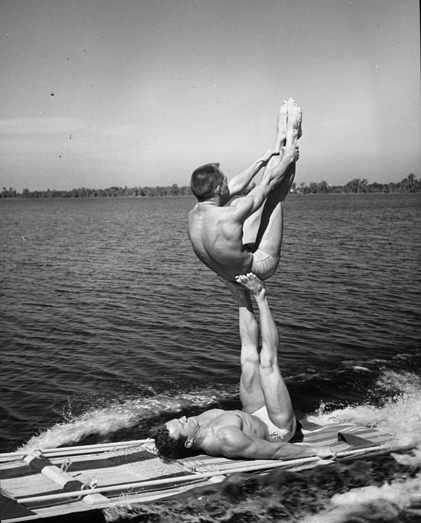 Two athletes practising a gymnastic 'aqua acrobatic' exercise on a water toboggan at Cypress Gardens, 1963
