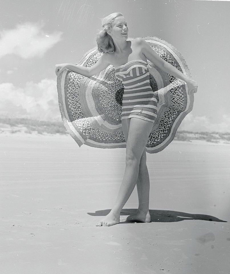 Pretty Ann Stolz, Cypress Gardens Aquamaid, takes off her wide brimmed sombrero to enjoy the sun at Daytona Beach.