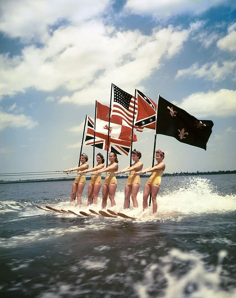A group of acrobatic water skiers holding flags perform during a show at Cypress Gardens theme park in 1953 near Winterhaven, Florida.