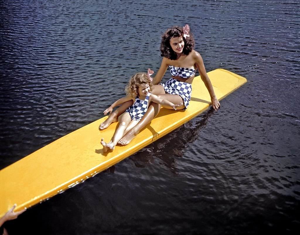 A southern belle model and a young girl in matching bathing suits relax on a surf board between shows at Cypress Gardens theme park in 1953 near Winterhaven, Florida.