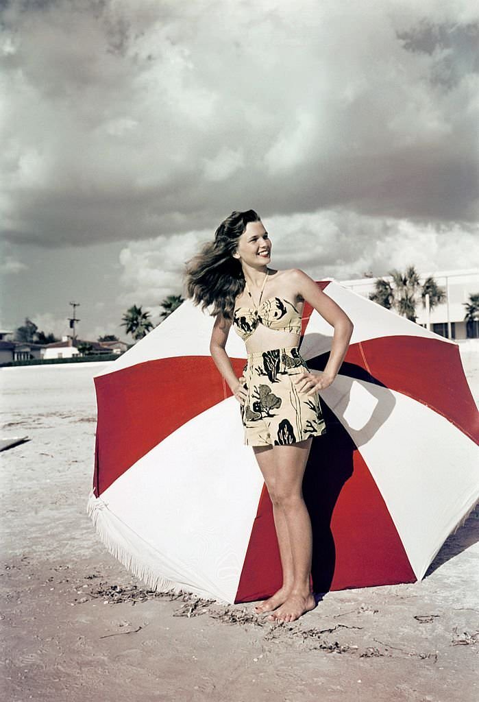 A southern belle model poses with an umbrella on the beach at Cypress Gardens theme park in 1953 near Winterhaven, Florida.