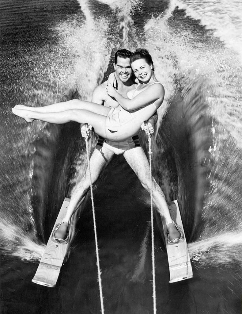 Kathy Darlyn and Trammell Pickett (water skiing stars) on skis; Pickett carries Darlyn in arms at Cypress Gardens, Florida, 1952