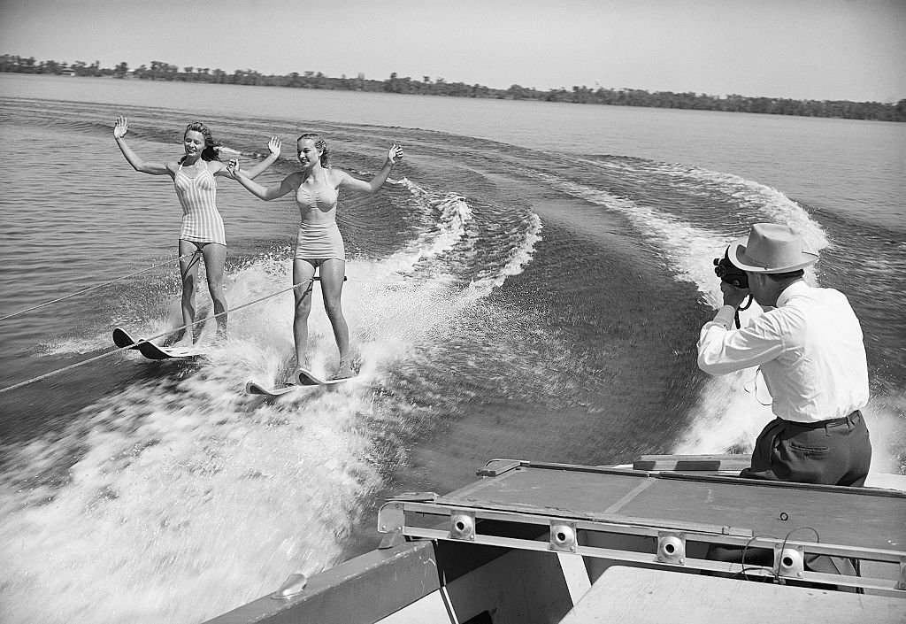 A man photographs two water skiing women on Lake Eloise, at Cypress Gardens, 1950's.