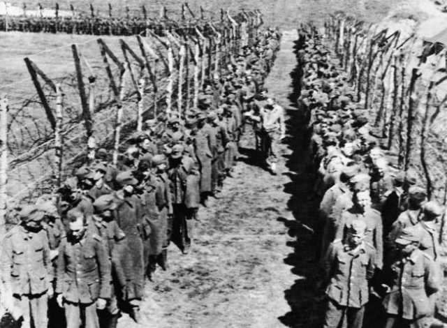 Two long double lines of German prisoners are checked by Allied officers, center, as they stand beside barded wire fences of compound in England, June 12, 1944, after their capture on the Normandy coast of France.