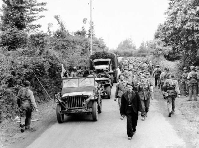 American troops moving up to the front lines, right, pass a long line of German prisoners marching back to a holding camp prior to being shipped out of France, on June 12, 1944.