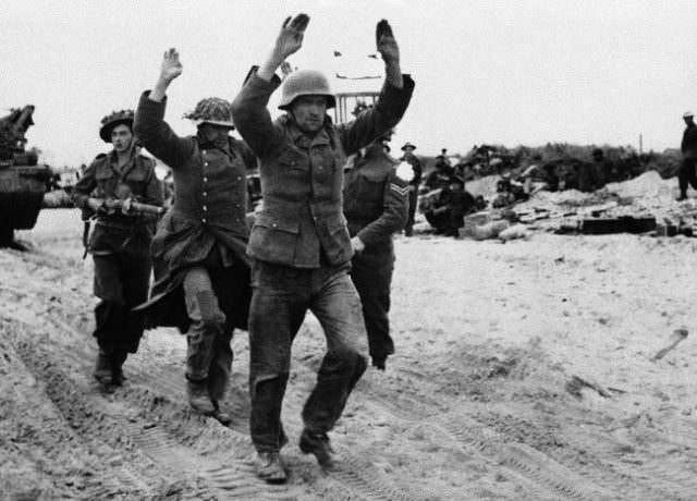 First the troops wade ashore from landing craft. Then the gradual development of land operations some of these early stages. German prisoners being marched along beach on June 11, 1944.