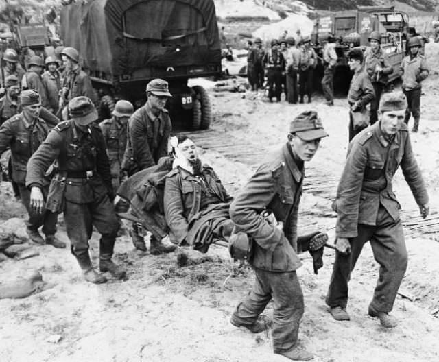 German prisoners of war, in the battle for France, carry a wounded comrade to an evacuation area on the beach where landing craft will speed them out to ships in the English Channel for treatment by Allied doctors on June 15, 1944.