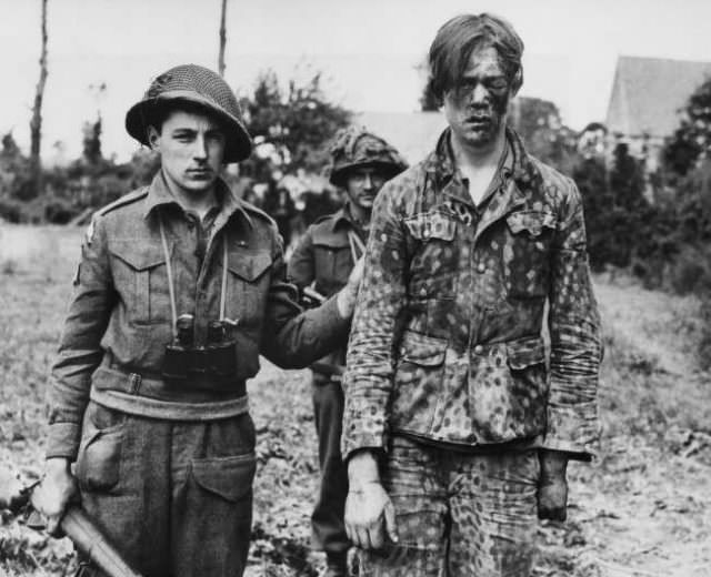 A wounded German prisoner, wearing a camouflages uniform, is escorted to an allied first aid station in France on June 21, 1944