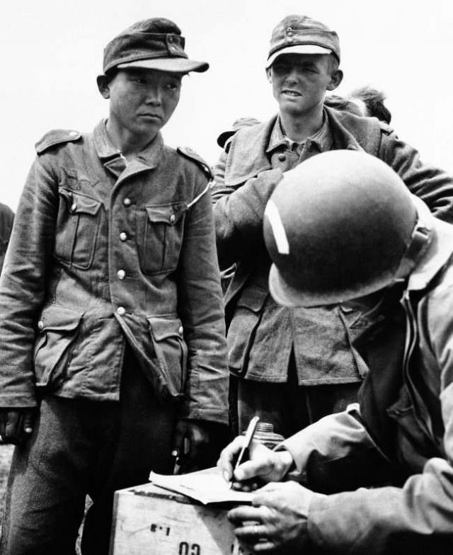 This Japanese, captured while serving in the German army in France on June 21, 1944, gives his name and serial number to an American as he files along with other German prisoners rounded up in the Normandy coast area.