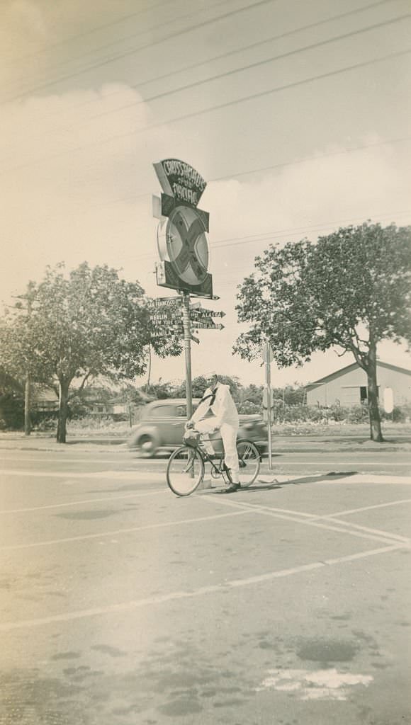Sailor on bicycling in front of Crossroads of the Pacific sign, 1940s
