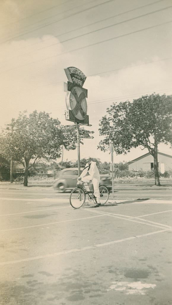 Sailor on bicycling in front of Crossroads of the Pacific sign, 1940s
